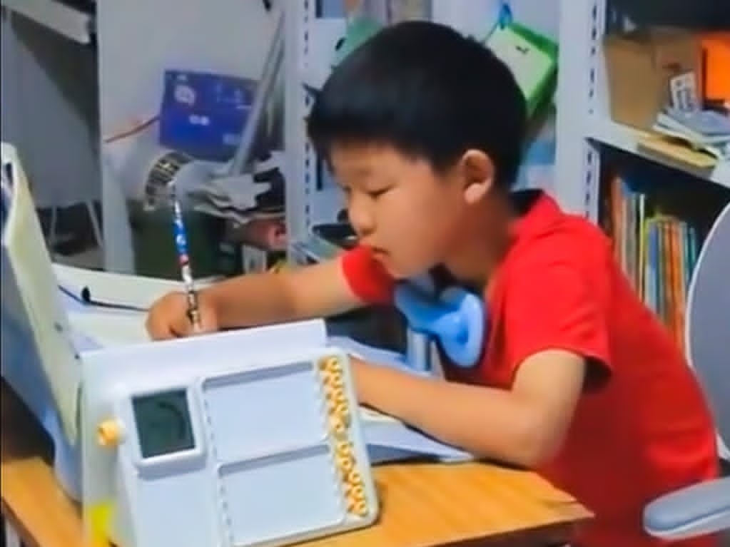 Cậu bé vừa đạp máy khâu, vừa làm bài tập về nhà